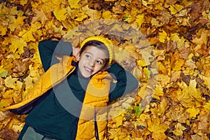 portrait of a fashionable baby boy in a yellow vest and hat in autumn lying in orange leaves in the afternoon on the