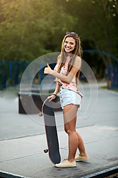 Portrait of fashionable beautiful young woman with a skateboard in a colorful dress in skatepark outdoors