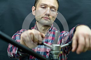 Portrait of a fashionable bicycle mechanic in a workshop on a black background. A young mechanic holds in his hands a professional