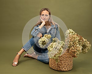 Portrait of Fashionable blonde model 30-35 years old florist in denim posing on olive background in studio, dried