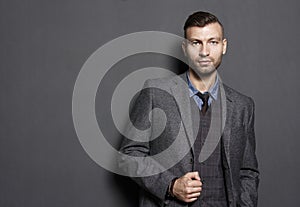 Portrait of fashionable confident handsome man in suit on gray wall background. Businessman looks seriously look