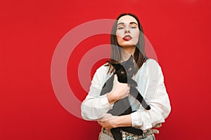 Portrait of a fashionable girl in light clothing posing with a cat in her hands on a red background, looking into the camera with