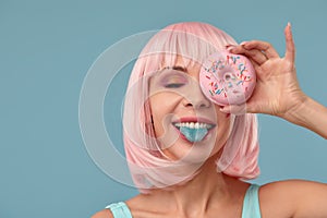 Portrait of a fashionable girl in a pink wig and with a pink donut in her hands keeps to the eye, shows tongue