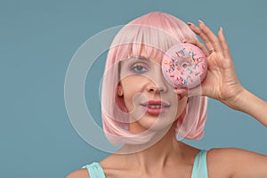 Portrait of a fashionable girl in a pink wig and with a pink donut in her hands keeps to the eye, shows tongue