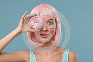 Portrait of a fashionable girl in a pink wig and with a pink donut in her hands keeps to the eye, shows tongue