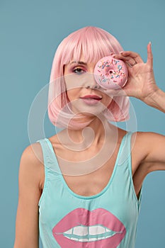 Portrait of a fashionable girl in a pink wig and with a pink donut in her hands keeps to the eye, shows tongue