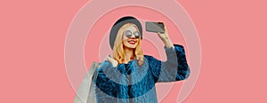 Portrait of fashionable happy smiling blonde woman taking selfie with mobile phone holds shopping bags wearing blue fur coat,