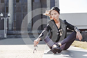 Portrait of fashionable impudent blonde girl with eye glasses wearing a rock black style outdoors in the city.