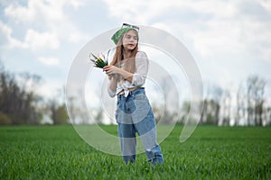 portrait of a fashionable little girl with a bouquet of wildflowers, in a green field, against a background of a cloudy