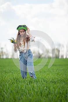 portrait of a fashionable little girl with a bouquet of wildflowers, in a green field, against a background of a cloudy