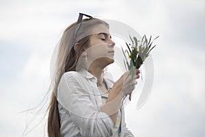 portrait of a fashionable little girl with a bouquet of wildflowers, in a green field, against a background of a cloudy