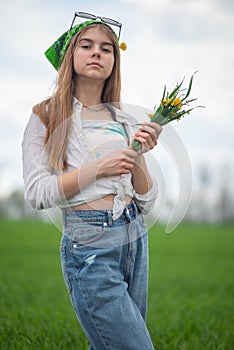 portrait of a fashionable little girl with a bouquet of wildflowers, in a green field, against a background of a cloudy