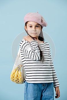 Portrait of a fashionable little girl in french beret holding bag with bananas