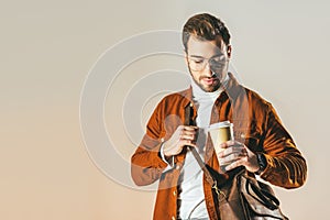 portrait of fashionable man with bag looking at disposable cup of coffee in hand