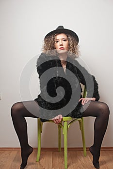 Portrait of a fashionable model with black fur sitting in a green chair in studio. Close up Portrait of young beautiful woman