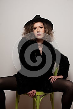 Portrait of a fashionable model with black fur sitting in a green chair in studio. Close up Portrait of young beautiful woman