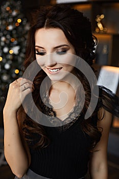 Portrait of a fashionable model girl with trendy hairstyle and trendy makeup in black blouse posing with festive lights