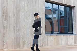 portrait of fashionable woman walking in city in coat wearing black cap.