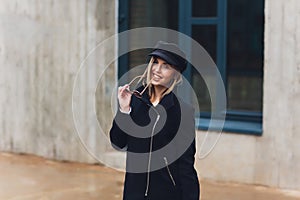 portrait of fashionable woman walking in city in coat wearing black cap.