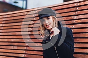 portrait of fashionable woman walking in city in coat wearing black cap.