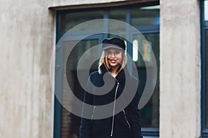 portrait of fashionable woman walking in city in coat wearing black cap.