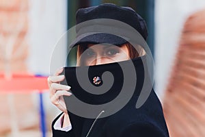 portrait of fashionable woman walking in city in coat wearing black cap.