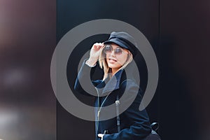 portrait of fashionable woman walking in city in coat wearing black cap.