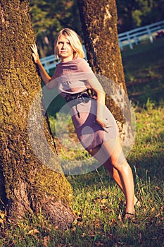 Portrait of fashionable young sensual blonde woman in garden enyoing on the grass field at sunset