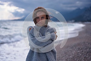 Portrait of fashionable young woman posing in high collar knitted sweater on sea background. Front view of sensual