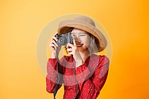 Portrait of fashionable young woman with vintage film camera for travelling concept. Isolated on orange background