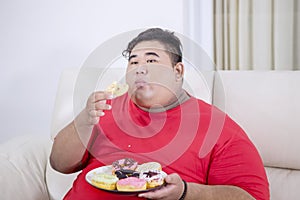 Portrait of fat Asian man eating doughnuts in home