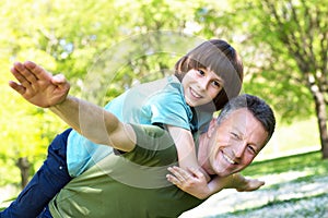Portrait of father with his son having fun in summer park. Piggyback. Family fun. Happy boy playing with dad summer outdoor