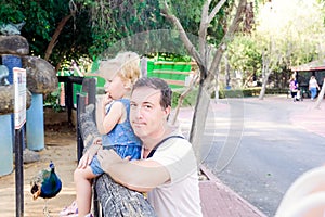 Portrait of father holding his toddler daughter looking to the nature in the zoo park. Family rest, spending time together concept