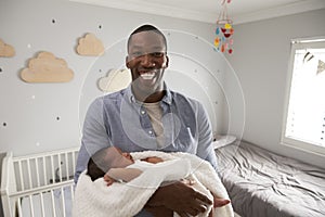 Portrait Of Father Holding Newborn Baby Son In Nursery