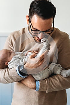 Portrait of a father hugging and kissing newborn baby. Authentic lifestyle touching tender moment.