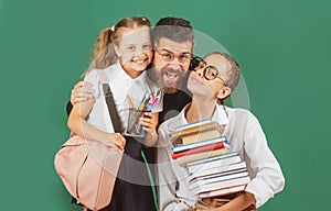 Portrait of father and school kids daughters hugging on blackboard background. Reading book and writing. Dad teaching