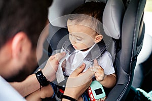 Portrait of young father securing baby in child seat of car