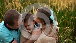 Portrait of father with son and daughter wrapped in blanket who sit in summer wheat field in slowmo