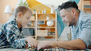 Portrait of father and son playing chess putting chessmen on board getting ready for game