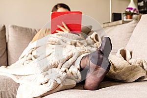 A portrait of the feet of a woman in black nylon stockings or pantyhose with reinforced toes lying in a couch under a cosy blanket