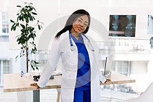 Portrait of a female African doctor in medical uniform posing in bright modern hospital