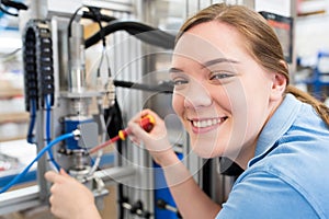 Portrait Of Female Apprentice Engineer Working On Machine In Factory