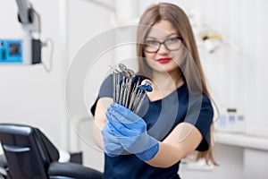 Portrait of female attractive dentist holding dental tools - at the modern dental office