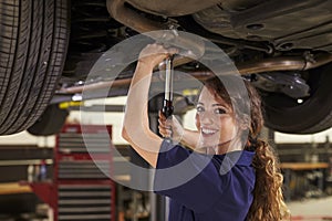 Portrait Of Female Auto Mechanic Working Underneath Car