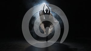 Portrait of female on black background under spotlight projector in studio. Ballerina in white tulle dancing slow