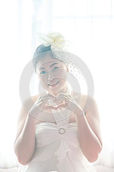 Portrait female bride with hands shaping a heart symbol on window white background