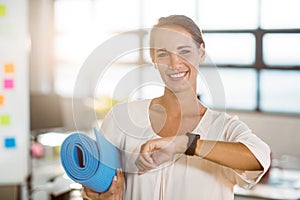 Portrait of female business executive holding exercise mat