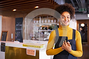 Portrait Of Female Business Owner Of Coffee Shop In Mask Using Digital Tablet During Health Pandemic photo