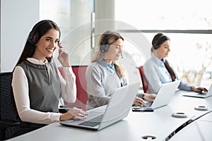 Portrait of female call center worker accompanied by her team. Smiling customer support operator at work.