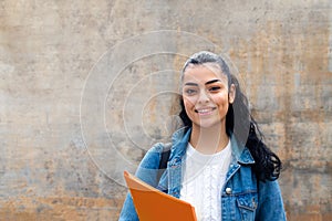 Portrait of female caucasian college student looking at camera carrying folders and a backpack. Copy space.